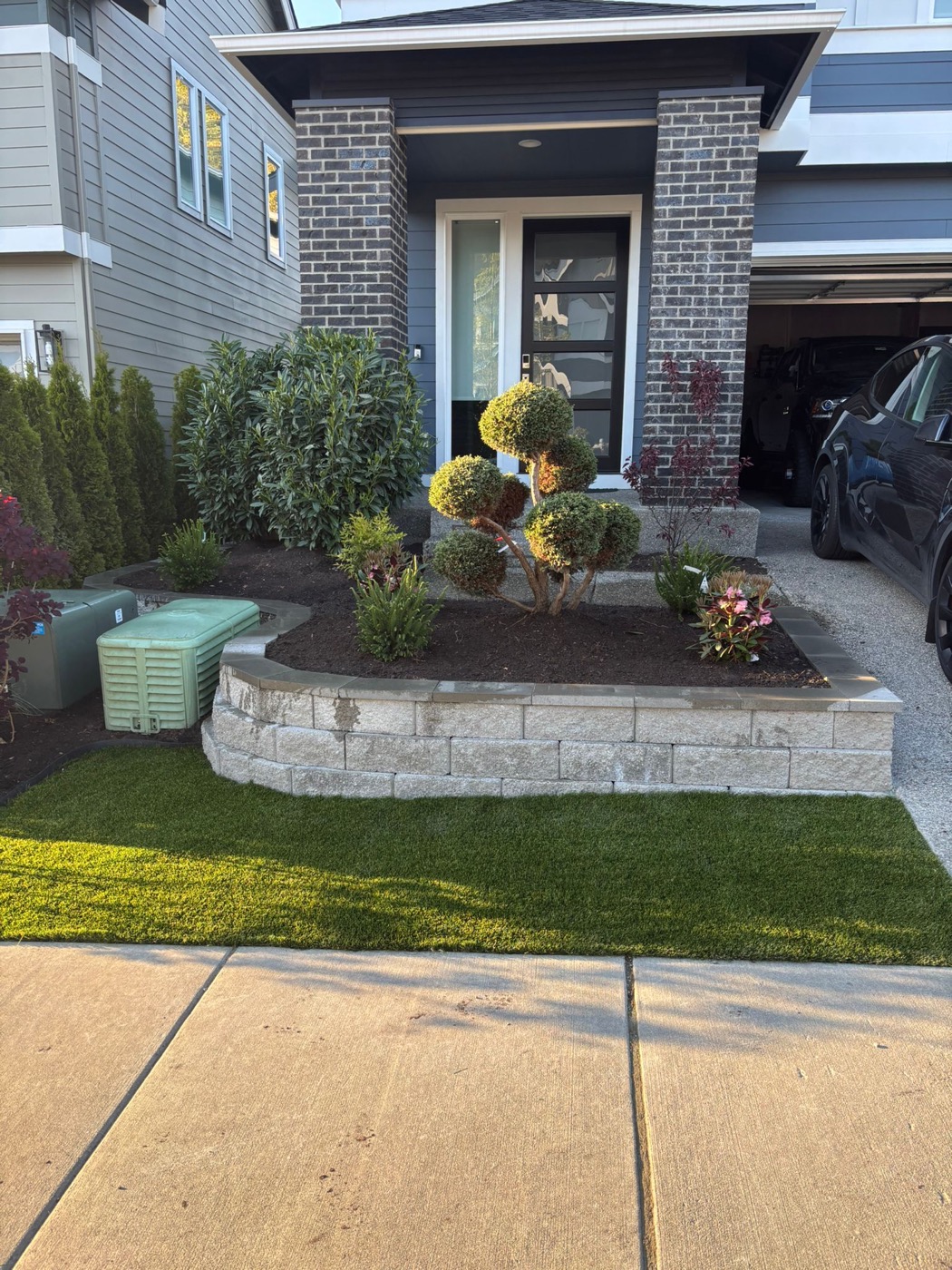 Front entry planting bed with trimmed shrubs, mulch, lawn, and stone border