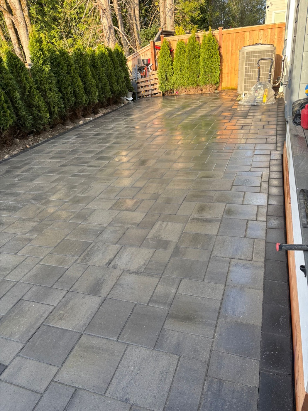 Clean paver patio next to privacy hedges and a wood fence