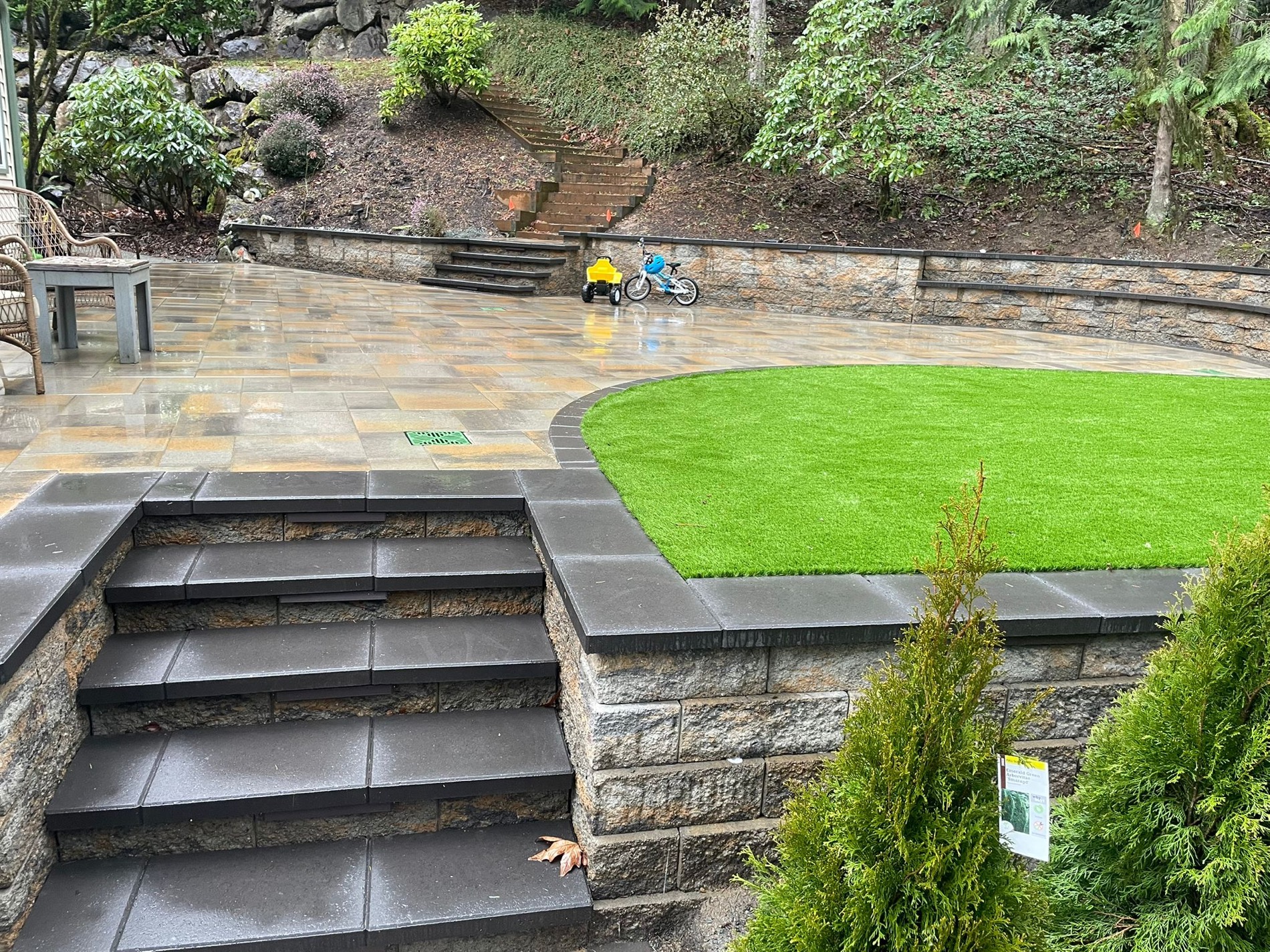 Wide finished backyard with paver patio, turf, stone wall, and steps